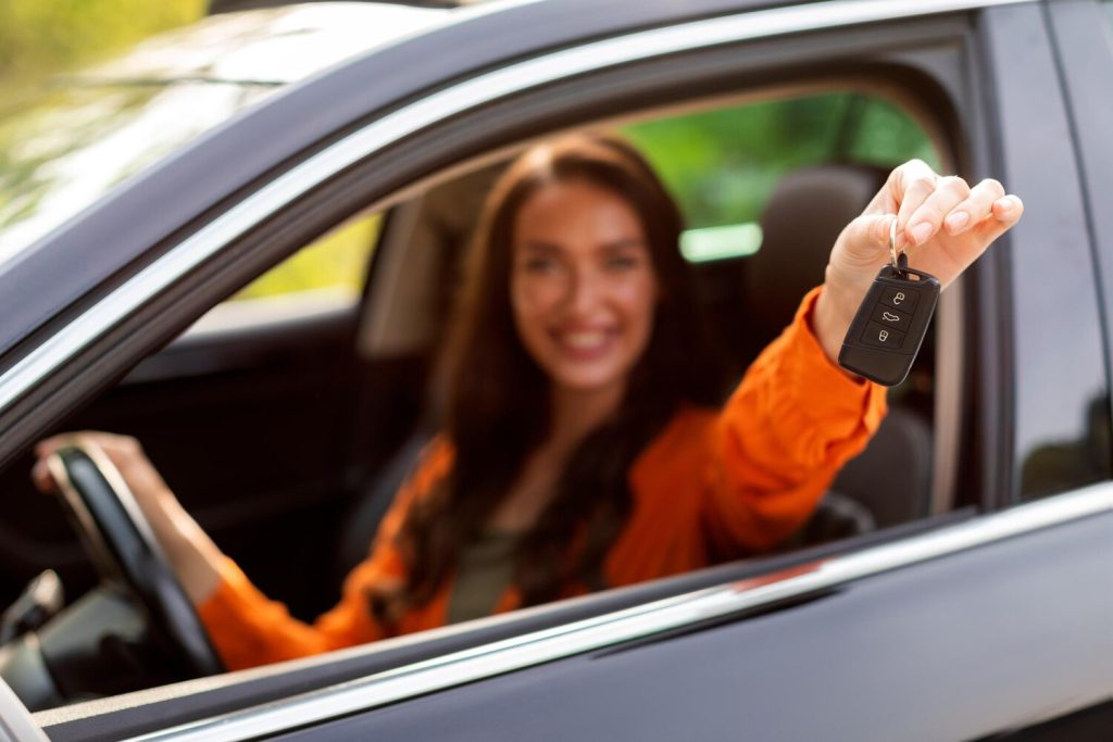 Test drive new car smiling lady showing automobile keys out of window sitting in vehicle on drivers