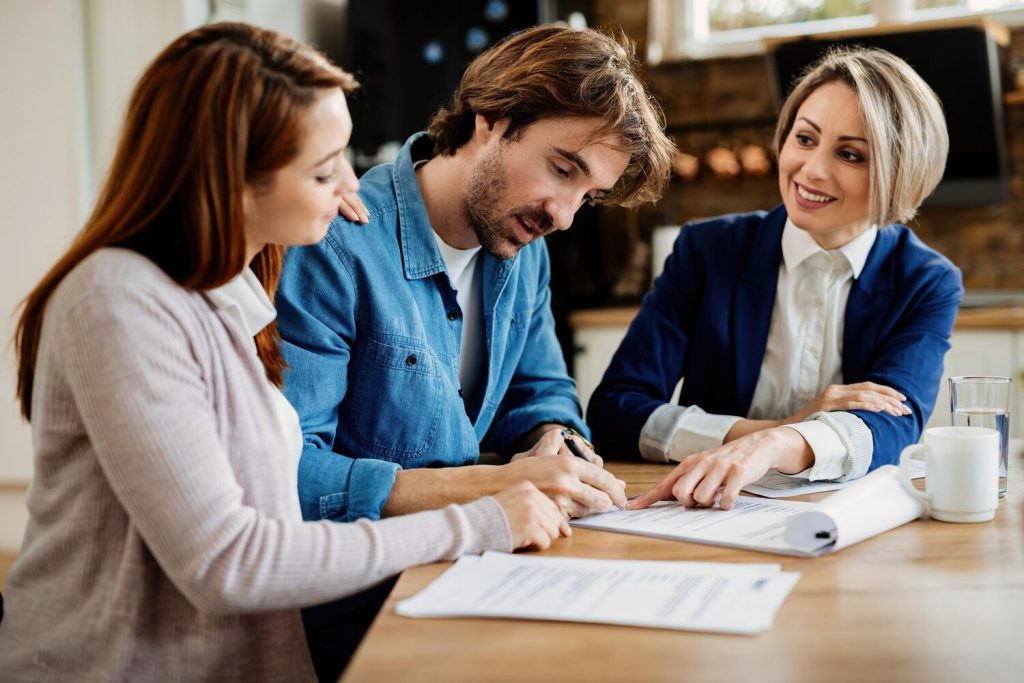 young couple signing lease agreement while having meeting with real estate agent focus is on man