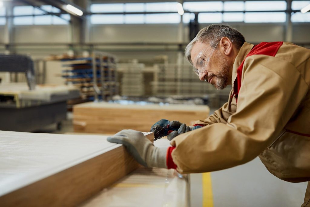 male worker using a drill while making furniture in carpentry workshop