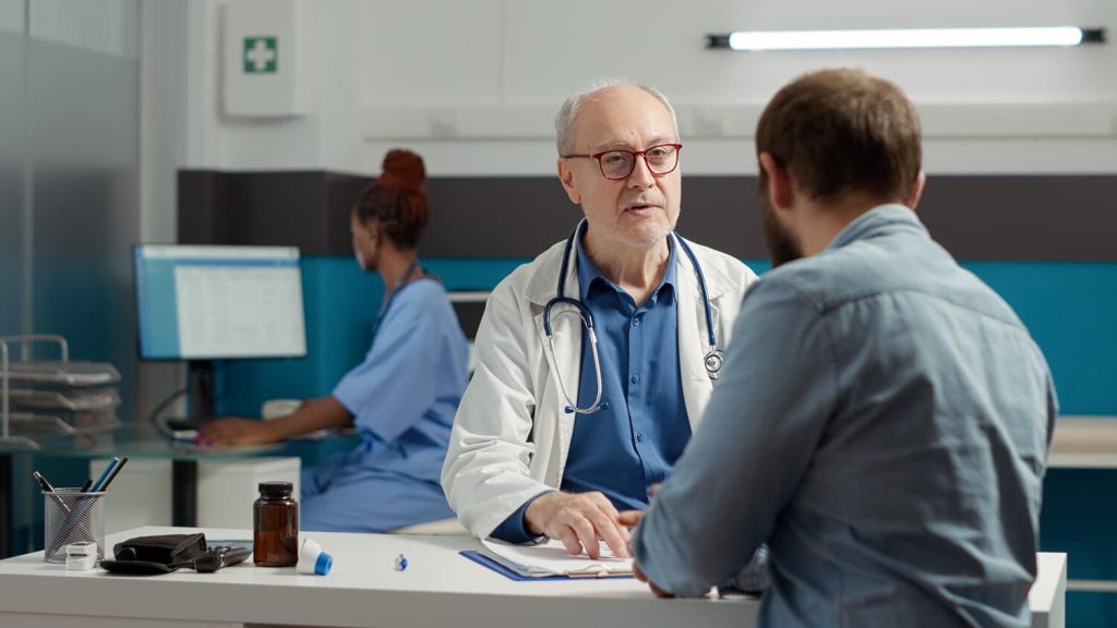 senior doctor doing health care consultation with young adult, talking about illness diagnosis and recovery treatment in office. having discussion about disease painkillers and medication.