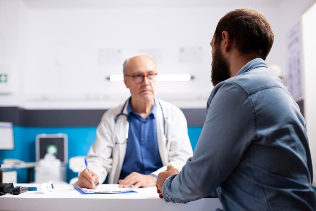 old physician listens to man in clinic