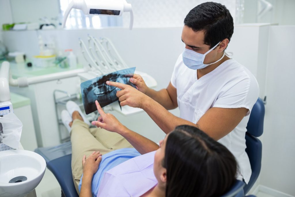young male dentist examining x-ray with the female patient