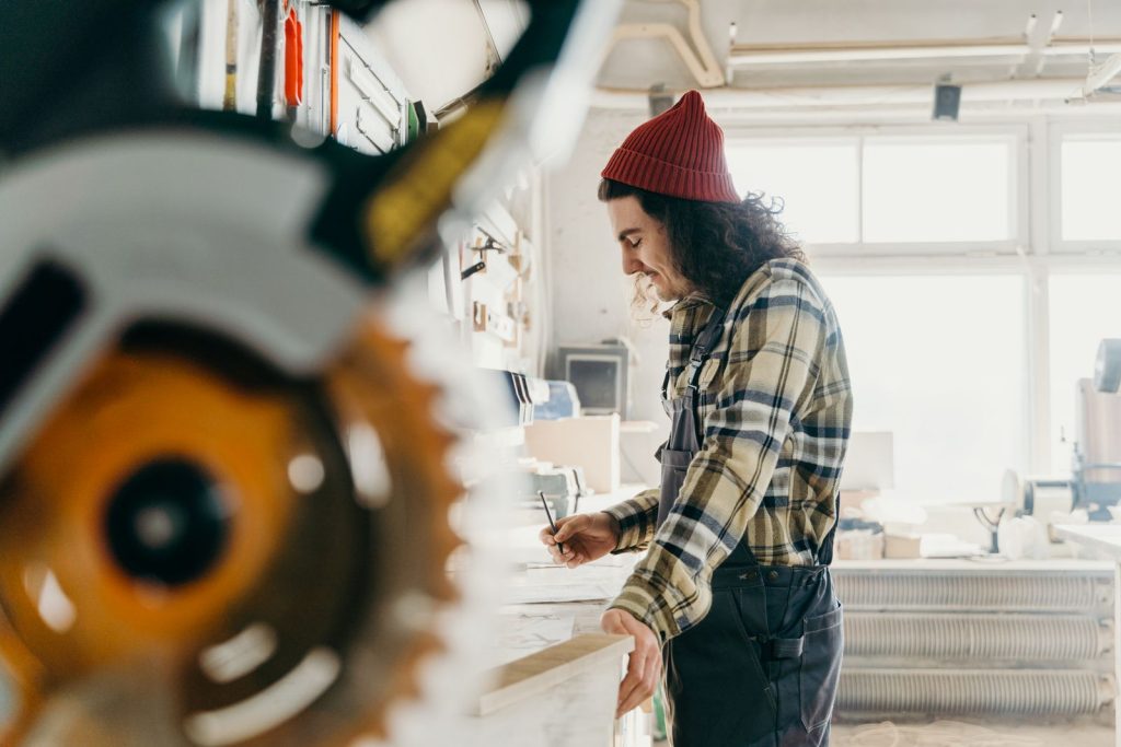 Un artisan mesure une pièce de bois dans son atelier.